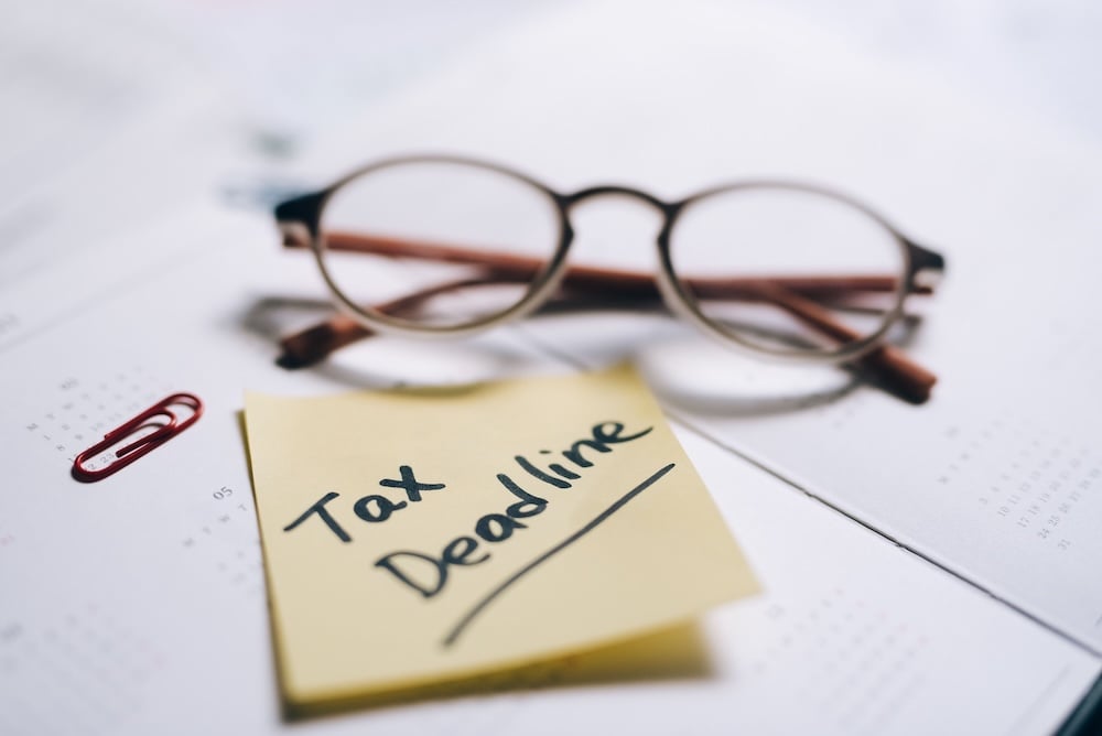 sticky note that syas tax deadline and pair of glass on desk